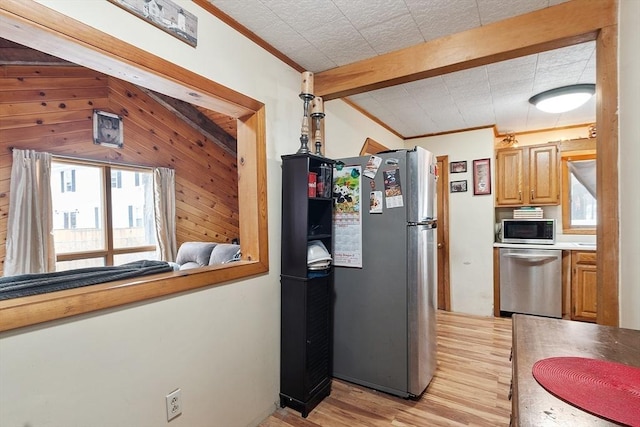 kitchen with stainless steel appliances, wooden walls, light wood-style flooring, and ornamental molding