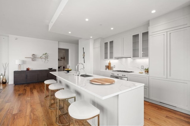 kitchen with sink, white cabinetry, a kitchen breakfast bar, an island with sink, and light wood-type flooring