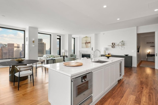 kitchen with sink, white cabinets, light stone counters, a center island with sink, and light wood-type flooring