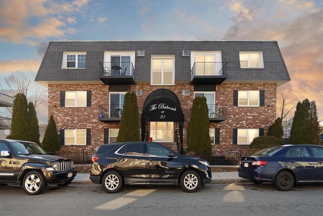 multi unit property featuring brick siding, mansard roof, and a shingled roof