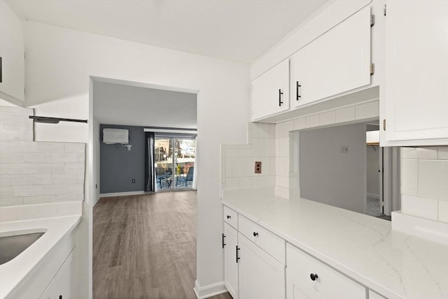 kitchen featuring light stone counters, backsplash, wood finished floors, white cabinetry, and baseboards