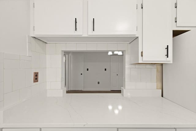 interior details with white cabinetry, light stone countertops, and backsplash