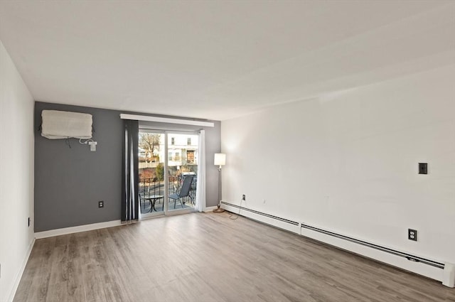 empty room featuring a baseboard heating unit, baseboards, and wood finished floors