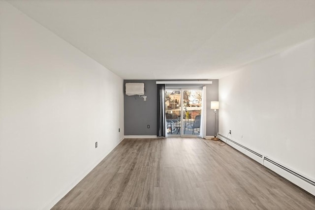 spare room with a wall mounted air conditioner, a baseboard radiator, baseboards, and wood finished floors