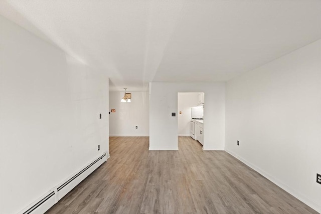 unfurnished room with a baseboard heating unit, baseboards, and light wood-style flooring