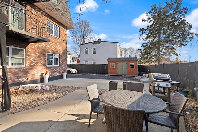 view of patio / terrace with an outbuilding, a storage unit, outdoor dining area, and a fenced backyard