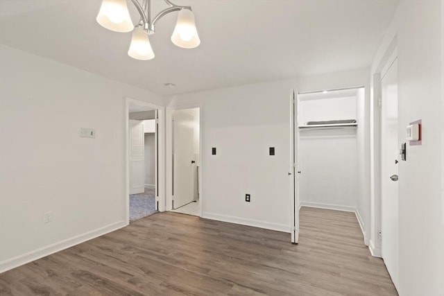 unfurnished bedroom featuring a walk in closet, wood finished floors, a closet, an inviting chandelier, and baseboards