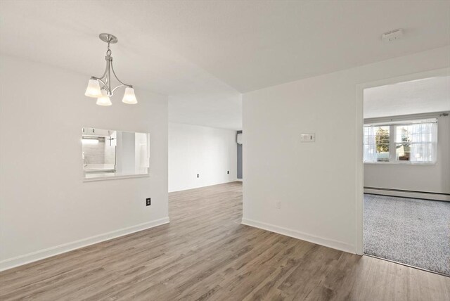 empty room featuring a baseboard heating unit, baseboards, and wood finished floors