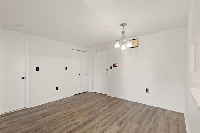 spare room with baseboards, an inviting chandelier, and wood finished floors