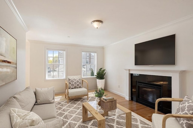 living room featuring a glass covered fireplace, wood finished floors, ornamental molding, and baseboards