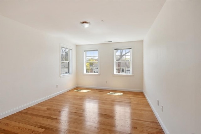 spare room featuring light wood finished floors, visible vents, and baseboards