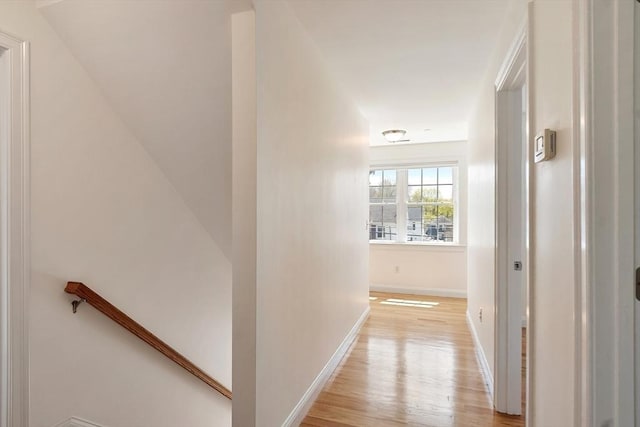 hallway with an upstairs landing, light wood-style flooring, and baseboards