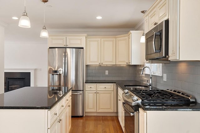 kitchen with light wood finished floors, a sink, stainless steel appliances, cream cabinetry, and dark countertops