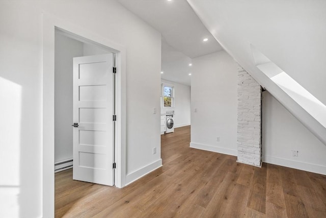 additional living space featuring washer / clothes dryer, a baseboard heating unit, and light hardwood / wood-style flooring