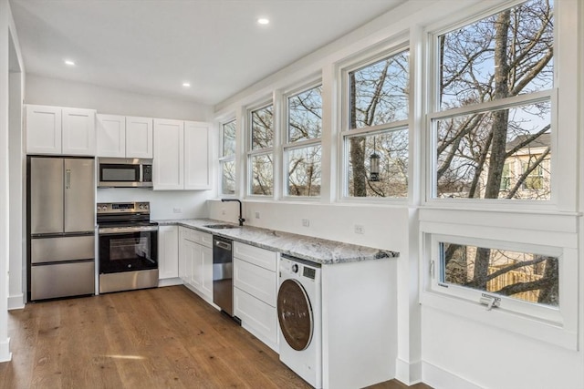 kitchen with sink, appliances with stainless steel finishes, white cabinetry, light stone countertops, and washer / dryer