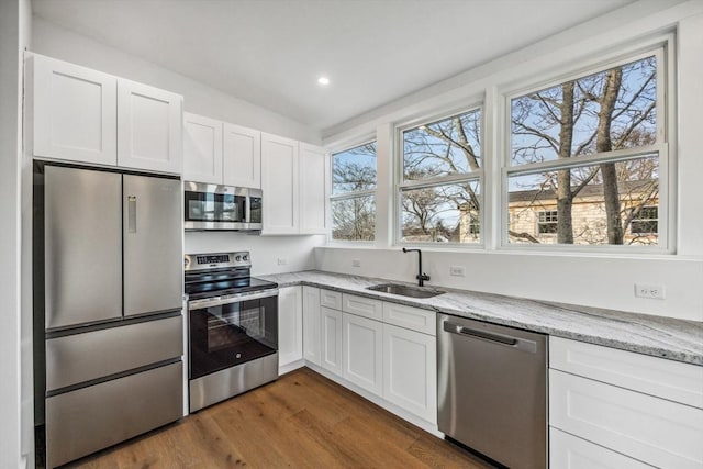 kitchen featuring white cabinetry, appliances with stainless steel finishes, sink, and light stone counters