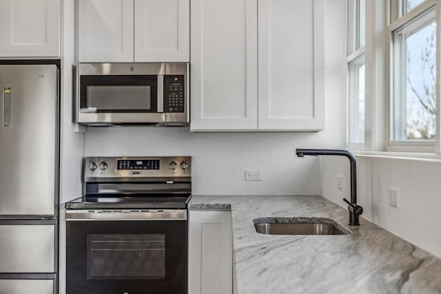 kitchen featuring white cabinetry, sink, light stone countertops, and appliances with stainless steel finishes