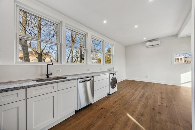 kitchen with an AC wall unit, washer / dryer, sink, white cabinets, and stainless steel dishwasher