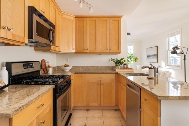 kitchen featuring kitchen peninsula, appliances with stainless steel finishes, light tile patterned flooring, light stone counters, and sink