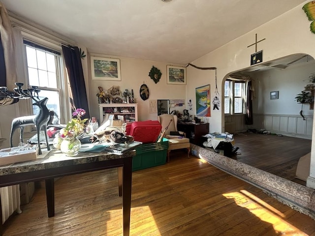 dining area featuring a wealth of natural light, arched walkways, wood-type flooring, and a wainscoted wall