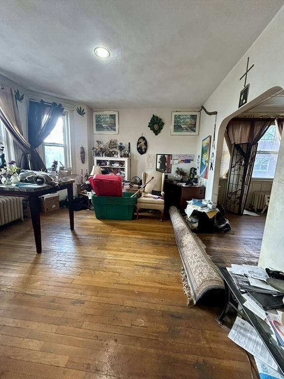 interior space with arched walkways, radiator, and hardwood / wood-style floors