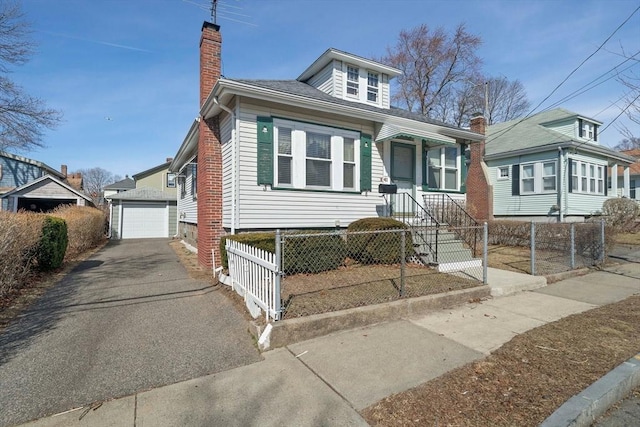 bungalow with driveway, a fenced front yard, a detached garage, an outdoor structure, and a chimney