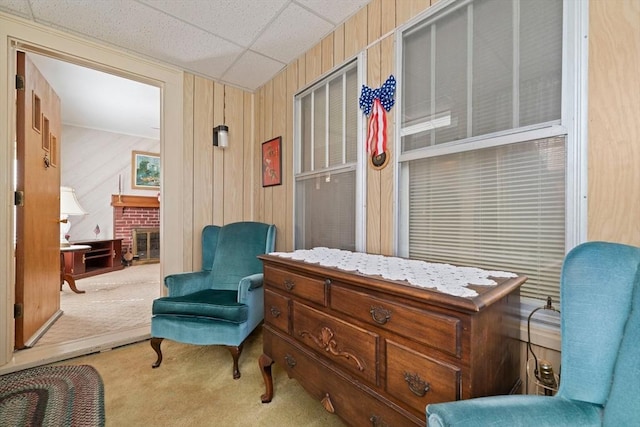 sitting room featuring a brick fireplace, a drop ceiling, and carpet floors