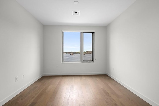 spare room featuring baseboards, visible vents, and wood finished floors