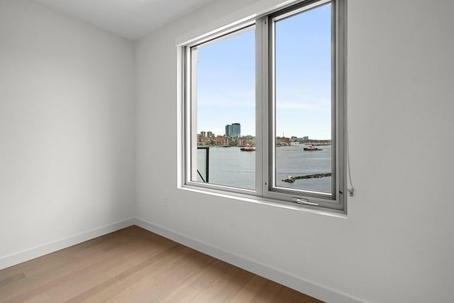 unfurnished room featuring baseboards, light wood-style floors, and a water view