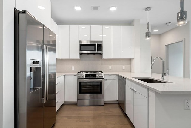 kitchen with a sink, stainless steel appliances, wood finished floors, white cabinets, and modern cabinets