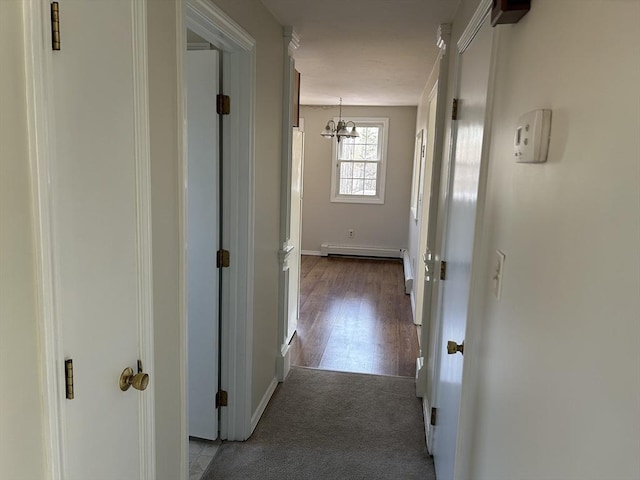 corridor with carpet floors, a baseboard radiator, wood finished floors, a chandelier, and baseboards