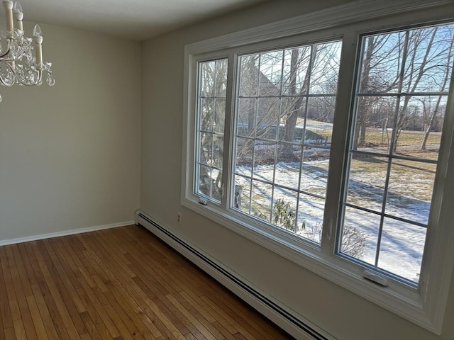 unfurnished dining area with an inviting chandelier, a baseboard radiator, baseboards, and wood-type flooring