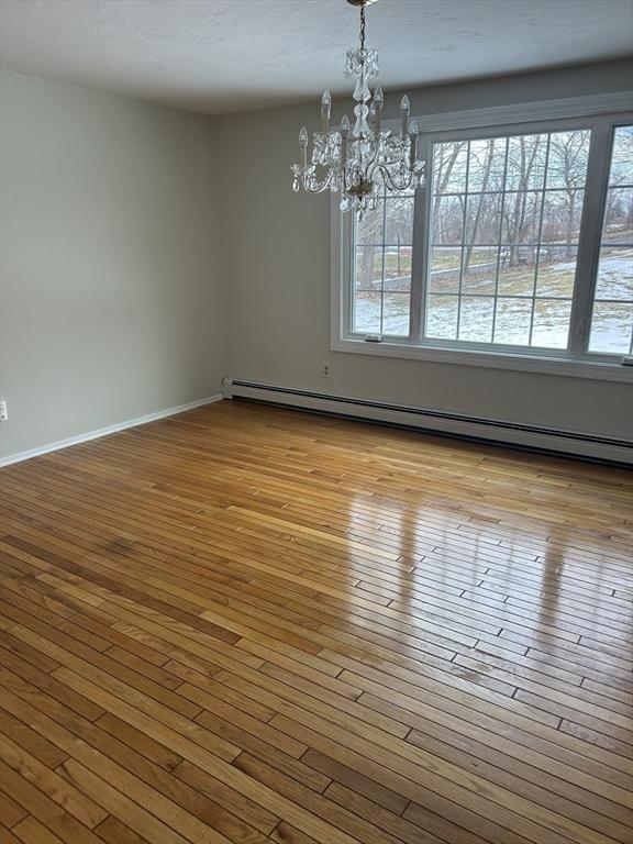 empty room featuring a baseboard radiator, baseboards, wood-type flooring, and a notable chandelier