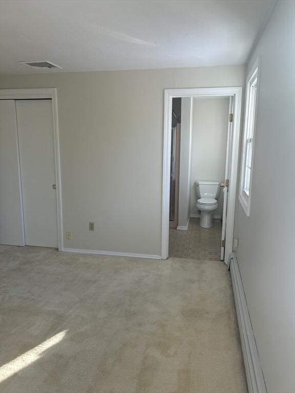 unfurnished bedroom featuring ensuite bathroom, a baseboard radiator, light colored carpet, visible vents, and a closet