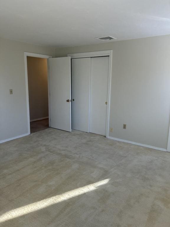 unfurnished bedroom featuring baseboards, a closet, visible vents, and light colored carpet