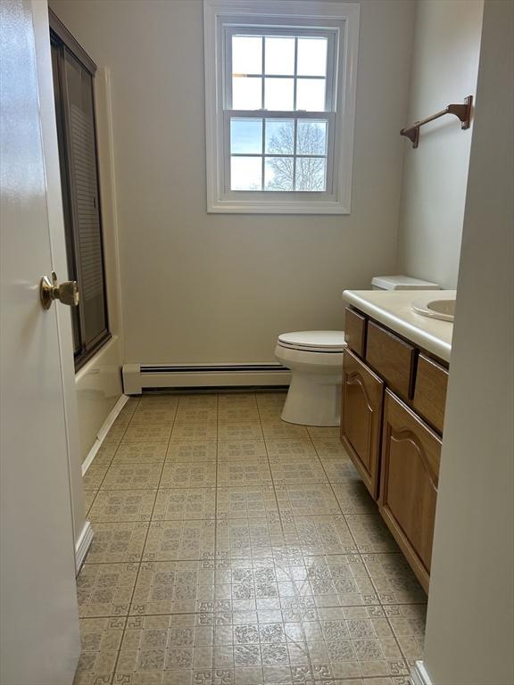 bathroom with a baseboard heating unit, combined bath / shower with glass door, vanity, and toilet