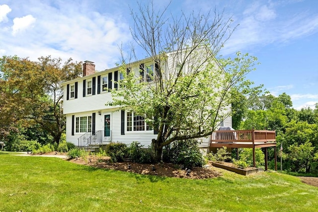 colonial inspired home featuring a chimney, a front lawn, and a wooden deck