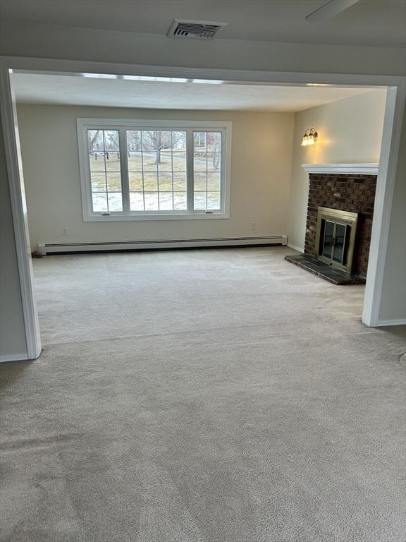 unfurnished living room featuring a wealth of natural light, visible vents, a baseboard heating unit, and carpet flooring