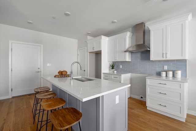 kitchen featuring a center island with sink, light hardwood / wood-style floors, sink, wall chimney range hood, and white cabinets