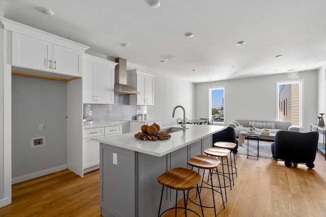 kitchen with light wood-type flooring, sink, wall chimney exhaust hood, a breakfast bar area, and a center island with sink