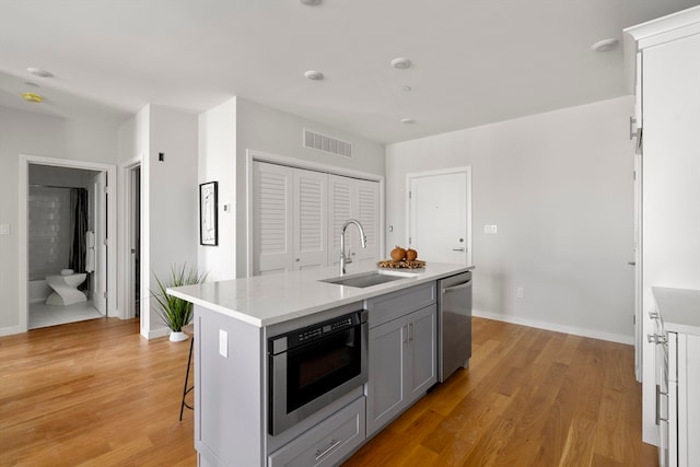 kitchen featuring a kitchen island with sink, light wood-type flooring, gray cabinets, stainless steel appliances, and sink