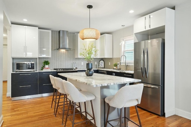 33 Century St Unit 3, Somerville, MA 02145 - kitchen featuring stainless steel appliances, wall chimney range hood, a kitchen breakfast bar, light wood finished floors, and pendant lighting