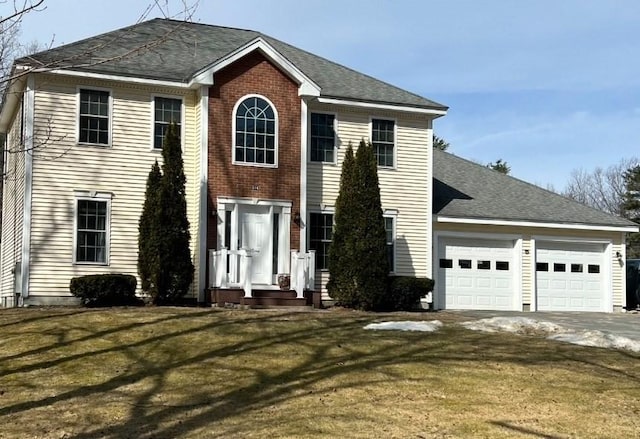 colonial-style house with brick siding, a shingled roof, a front yard, a garage, and driveway