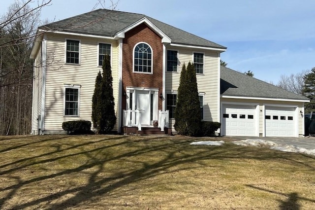 colonial house featuring brick siding, driveway, an attached garage, and a front lawn