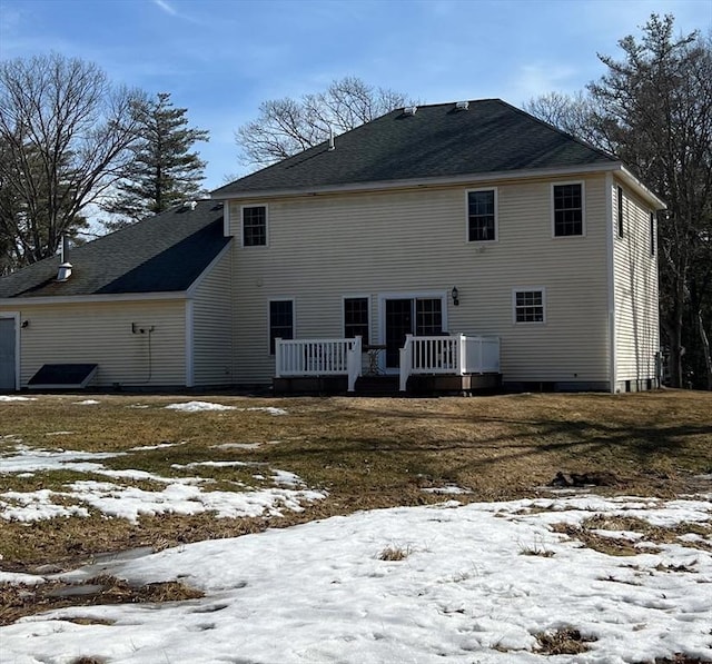 snow covered rear of property featuring a wooden deck and a shingled roof