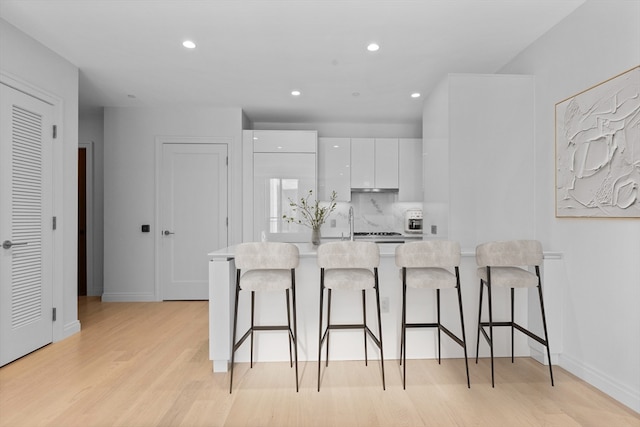 kitchen featuring white cabinetry, an island with sink, tasteful backsplash, light wood-type flooring, and a kitchen bar