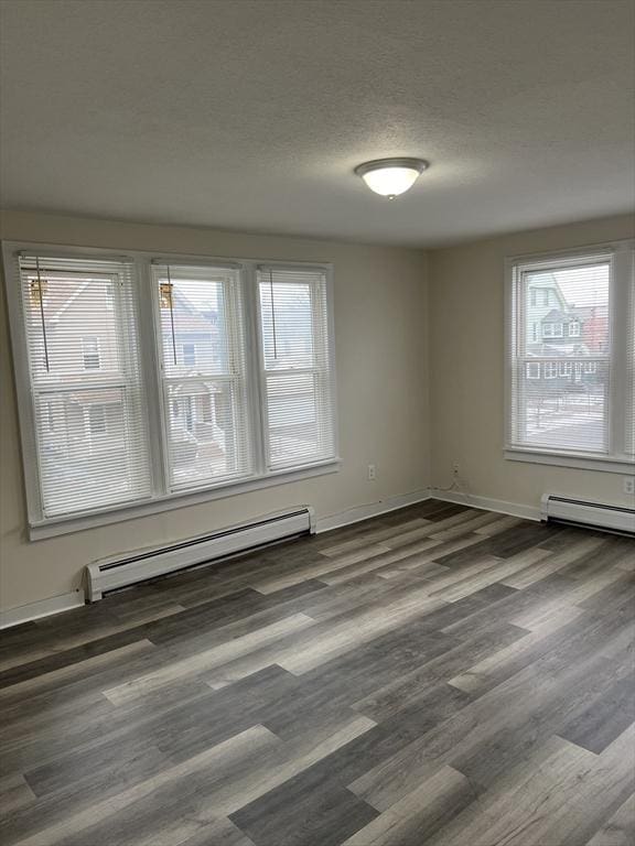 empty room with a baseboard heating unit, a textured ceiling, baseboards, and wood finished floors