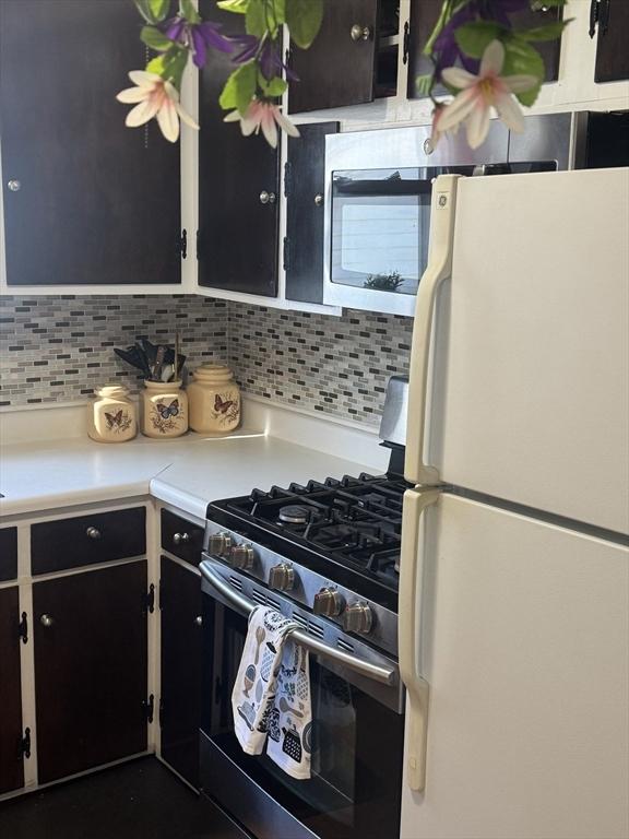 kitchen featuring white refrigerator, backsplash, and stainless steel gas range