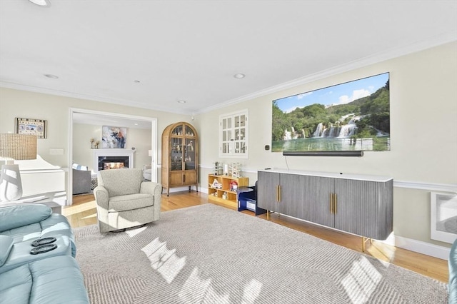 living room with a warm lit fireplace, light wood-type flooring, and ornamental molding