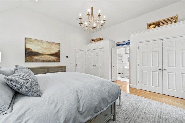 bedroom featuring lofted ceiling, ensuite bathroom, a chandelier, and wood finished floors